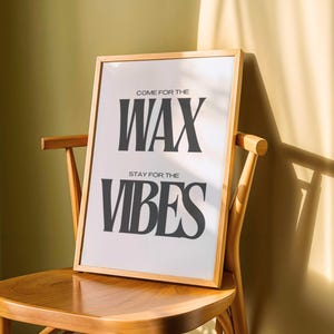 Puede incluir: Una l&aacute;mina rectangular con un marco de madera de color claro. El fondo blanco presenta un texto en negrita, gris oscuro y en may&uacute;sculas que dice: COME FOR THE WAX, STAY FOR THE VIBES. La l&aacute;mina est&aacute; colocada sobre una silla de madera.