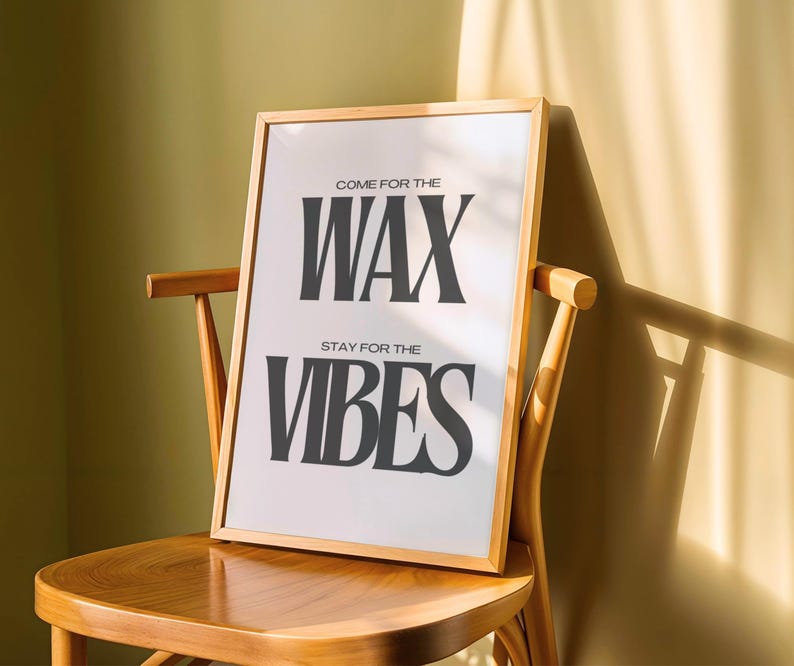 Puede incluir: Una l&aacute;mina rectangular con un marco de madera de color claro. El fondo blanco presenta un texto en negrita, gris oscuro y en may&uacute;sculas que dice: COME FOR THE WAX, STAY FOR THE VIBES. La l&aacute;mina est&aacute; colocada sobre una silla de madera.