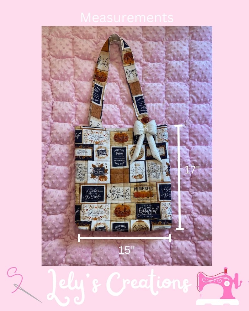 May include: A tote bag with a fall theme, featuring a patchwork design with pumpkins and the words "Give Thanks" and "Grateful." The bag is 15 inches wide and 17 inches tall, with a cream-colored bow and a patterned strap.