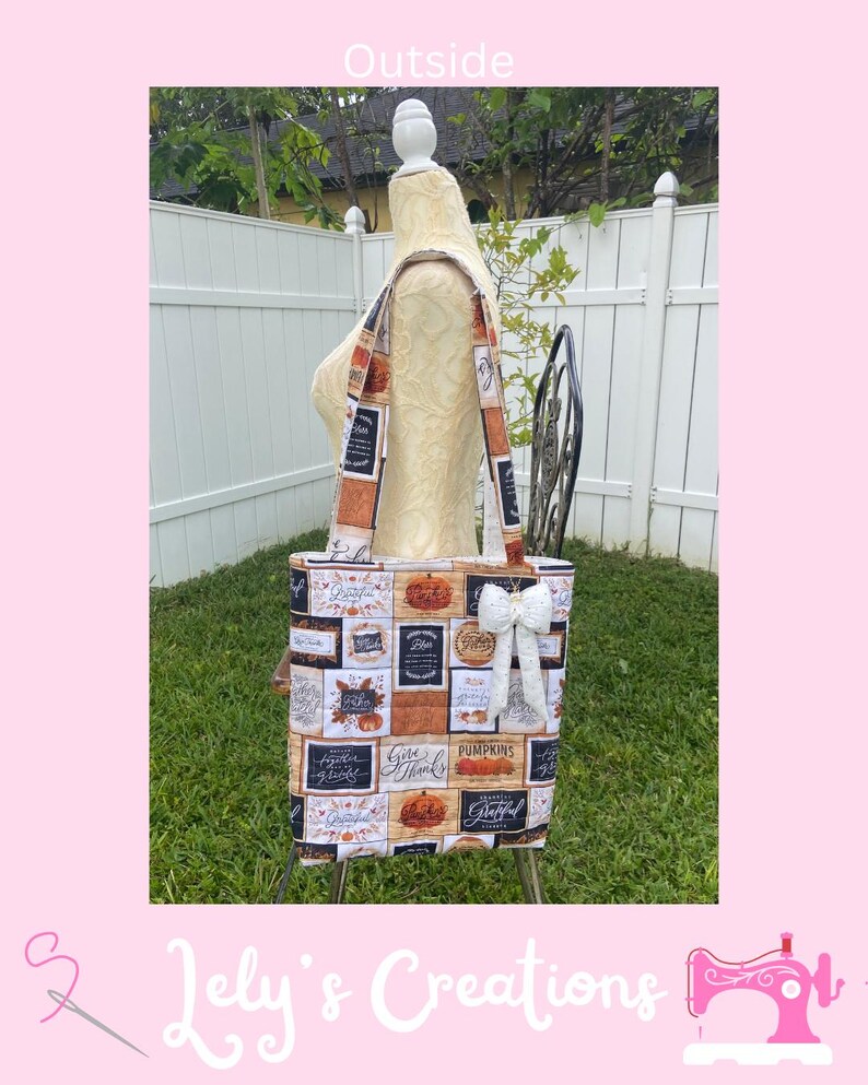 May include: A tote bag with a fall-themed patchwork design featuring pumpkins and the words "Give Thanks" and "Grateful." The bag has a white bow and is displayed on a mannequin. The bag's straps are also patterned.