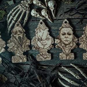 May include: A set of seven light-colored wooden air freshener-shaped ornaments featuring laser-engraved portraits of iconic horror movie characters, including a clown, a masked killer, a doll, and other figures, each with a hole at the top.