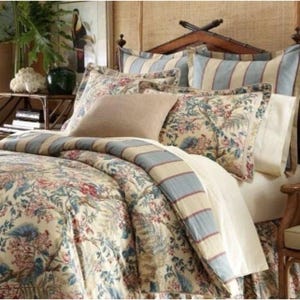 May include: A bed set featuring a floral patterned duvet cover and matching pillow shams in shades of blue, red, and green on a cream background. The bedding includes striped accent pillows and a solid tan square cushion on a wooden bed frame.