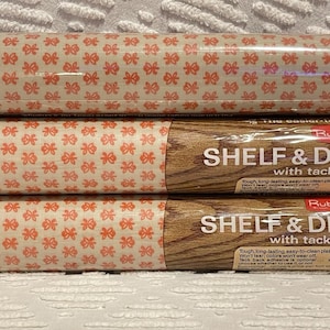 May include: Three rolls of shelf and drawer liner featuring a repeating orange floral pattern on a cream background. The packaging includes text reading SHELF & DRAWER with tack, highlighting features like tough, long-lasting, and easy-to-clean.