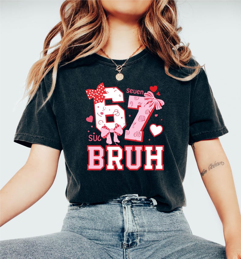 Puede incluir: Camiseta negra con un dise&ntilde;o gr&aacute;fico que presenta los n&uacute;meros "67" con lazos y corazones, y la palabra "BRUH" en rosa y blanco. La camiseta tiene las palabras "Seuen" y "s&uacute;c" encima de los n&uacute;meros.