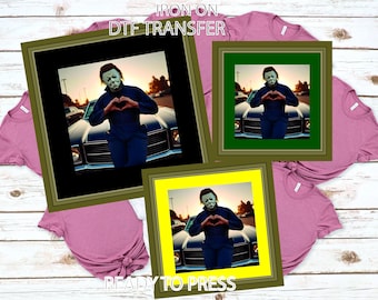 May include: DTF transfer featuring a framed image of a person in a mask making a heart shape with their hands. The image is surrounded by green, black, and yellow frames. The text "IRON ON DTF TRANSFER" and "READY TO PRESS" are visible.