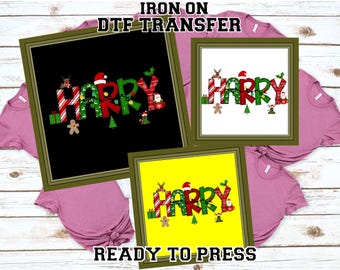 May include: Three framed Christmas-themed DTF transfer designs with the word "HAPPY" in red and green, decorated with festive elements. The transfers are ready to press and are displayed on pink t-shirts.