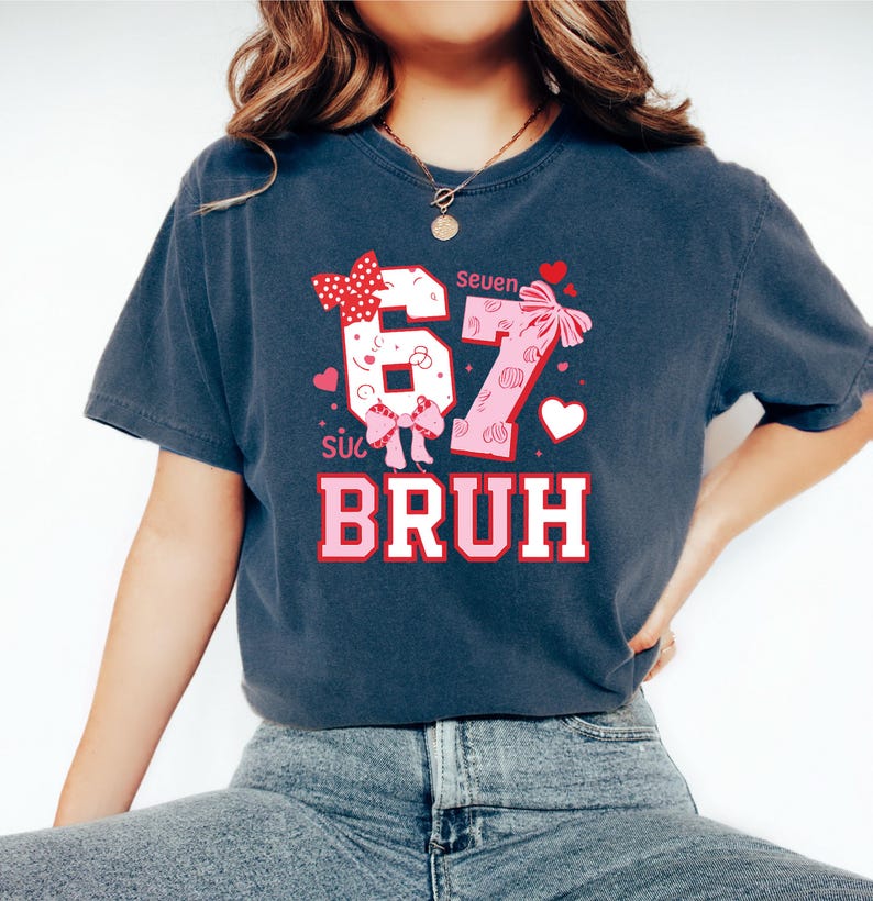 Puede incluir: Camiseta azul oscuro con un dise&ntilde;o gr&aacute;fico. El dise&ntilde;o presenta los n&uacute;meros "67" en rosa y blanco, con lazos y corazones. La palabra "BRUH" est&aacute; impresa en rosa y blanco debajo de los n&uacute;meros. La palabra "Seven" est&aacute; impresa encima de los n&uacute;meros.