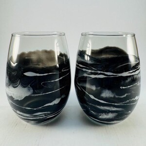 May include: A pair of stemless wine glasses with a black and white abstract design. The interior of each glass features a swirling pattern of black and white, resembling waves or clouds. The glasses are clear and have a smooth surface.