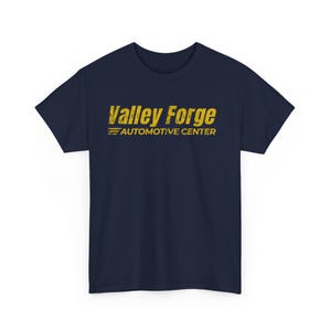 May include: Navy blue t-shirt with the text "Valley Forge Automotive Center" in distressed yellow lettering. The shirt is a classic crew neck style.