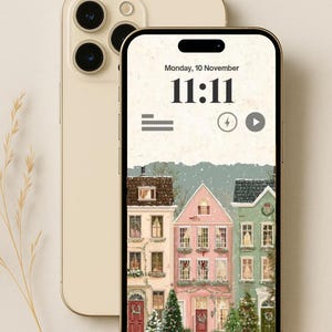 May include: A gold-colored smartphone displays a winter village scene with the time 11:11 on the screen. The wallpaper features colorful houses, Christmas trees, and falling snow. The phone's camera lenses are visible.