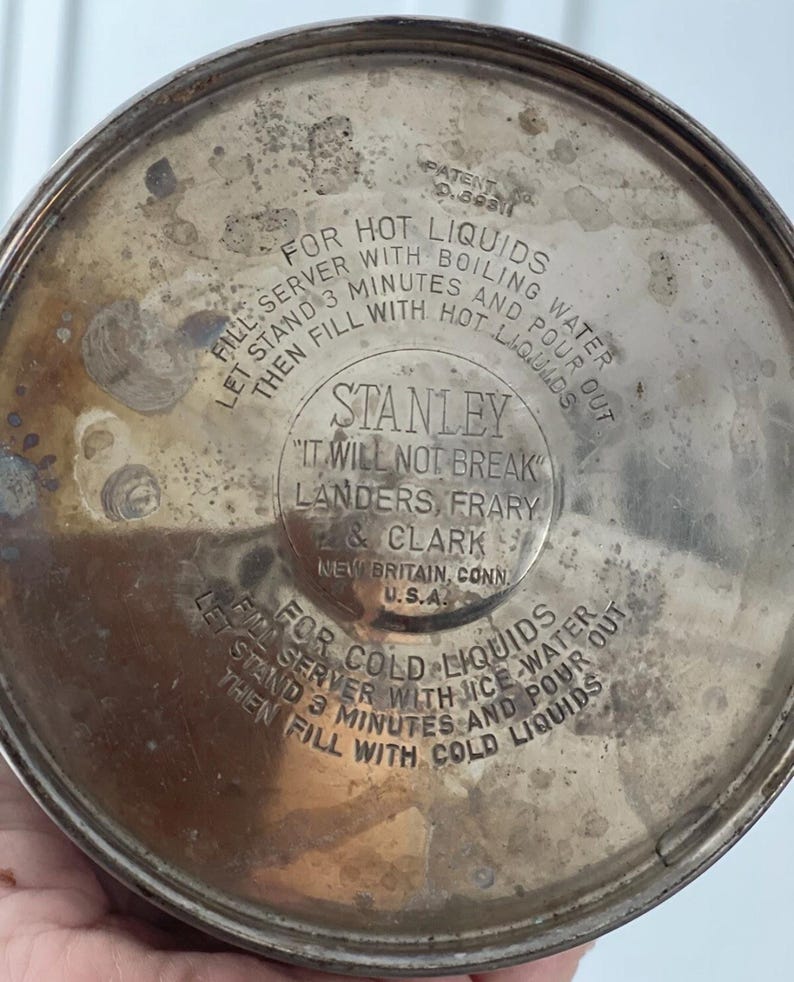 Puede incluir: Primer plano de la base de un termo Stanley vintage. La superficie met&aacute;lica plateada tiene el texto "Stanley, It Will Not Break". Tambi&eacute;n son visibles las instrucciones para l&iacute;quidos calientes y fr&iacute;os.