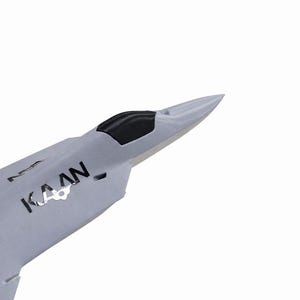 May include: A light gray model airplane with the word "KAAN" printed on the side. The plane has a black cockpit and a pointed nose. The image is set against a white background.
