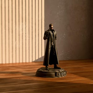 Puede incluir: Figura detallada de un hombre con un abrigo largo negro y gafas de sol, de pie sobre una base circular. La base tiene el texto "A WECKER". La figura está sobre un fondo neutro con sombras verticales.