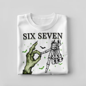 May include: White sweatshirt featuring a Halloween-themed graphic. The design includes the text "SIX SEVEN" above a green zombie hand and a skeleton hand making a gesture. Green bats and stars complete the design.