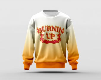 May include: White sweatshirt with an ombre design that fades from white to orange. The sweatshirt features the text "BURNIN' UP" in red and gold lettering, with a flame-like design. The cuffs and hem are solid orange.