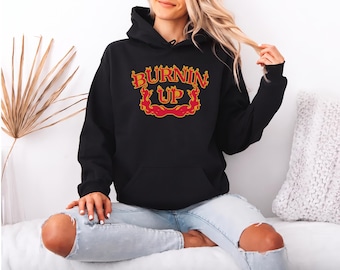 May include: A black hooded sweatshirt featuring the text BURNIN UP in a stylized yellow font with a red flame outline. The hoodie has long sleeves, a front kangaroo pocket, and a drawstring hood, providing a casual look with a graphic design.