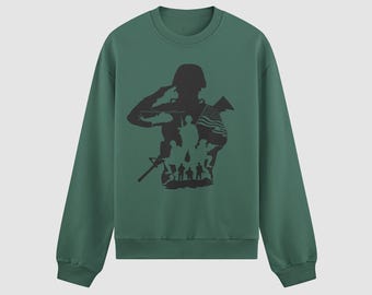 May include: A dark green sweatshirt featuring a black silhouette of a saluting soldier with a helicopter, American flag, and other soldiers. The design is centered on the front of the long-sleeved crew neck top.