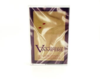 May include: A cassette tape with a cover featuring the title "The Immortal Kiss of the Vampire" in a stylized font. The cover has a gold and purple color scheme with two red dots. The text "Rich, Dark, Sensuous Music Inspired by an 18th Century Vampire" is also visible.