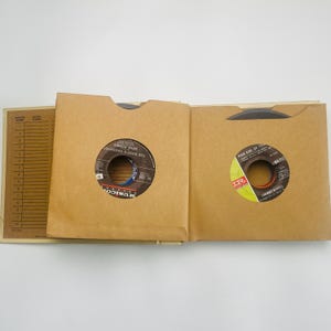 May include: An open record album with two vinyl records in brown paper sleeves. The record on the left is labeled "The Boss's Daughter" by Gene Pitney. The record on the right is labeled "Poor Side of Town" by Johnny Rivers.