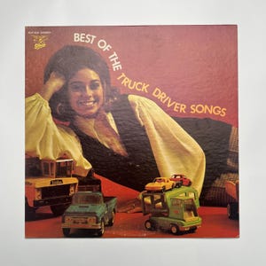 May include: Vintage vinyl record album cover titled "Best of the Truck Driver Songs." The cover features a woman and toy trucks. The album cover is red with the text in orange. The toy trucks are yellow, green, and blue.