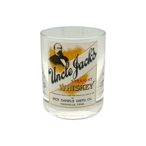 May include: A clear, cylindrical whiskey glass with a label featuring the text "Uncle Jack's STRAIGHT WHISKEY". The label includes a portrait of a man and the text "Jack Daniels Distg. Co., Nashville, Tenn."