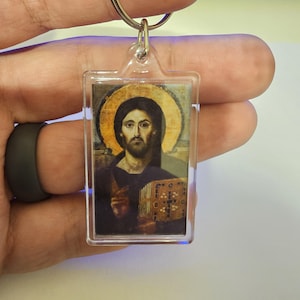 May include: Clear rectangular keychain featuring a religious icon of Jesus Christ. The image shows Jesus with a golden halo, dark hair, and a beard. The keychain has a silver metal ring.