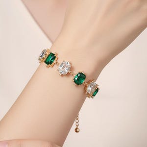 Goldfarbenes Metallarmband mit rechteckigen smaragdgrünen und kristallklaren Zirkonia-Steinen.