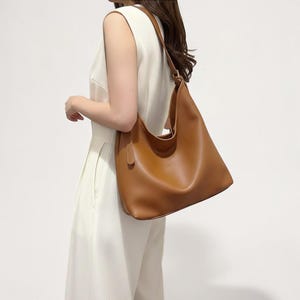 Puede incluir: Un bolso de hombro de cuero marrón claro con una sola correa. El bolso es de estilo suave y holgado con una forma redondeada. El bolso se lleva sobre el hombro.