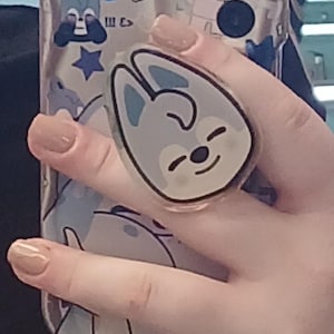 May include: Clear phone case with a cartoon design featuring a blue and white bunny and stars. A matching bunny phone grip is attached. The case has a three-lens camera cutout.
