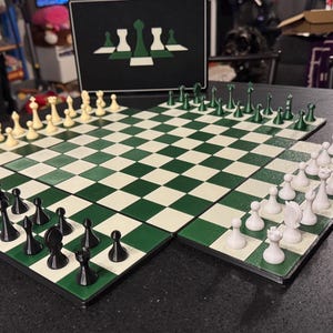 May include: A green and white checkered chess board with chess pieces set up for a game. The chess pieces are black, white, and green. A black and white image of chess pieces is in the background.