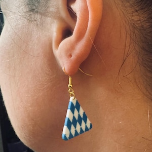 Puede incluir: Pendiente de gancho dorado con un patrón de diamantes azules y blancos. El pendiente tiene forma triangular y cuelga de la oreja. Esta joya única es una pieza de joyería.