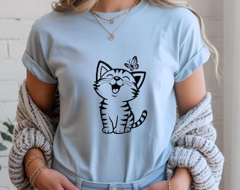 May include: Light blue t-shirt featuring a black and white cartoon cat with a butterfly. The cat is smiling with its mouth open. The shirt has rolled-up sleeves and is made of a soft material.
