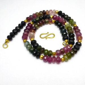May include: A multi-colored gemstone necklace with a gold clasp. The necklace is made of faceted beads in shades of pink, green, and black.