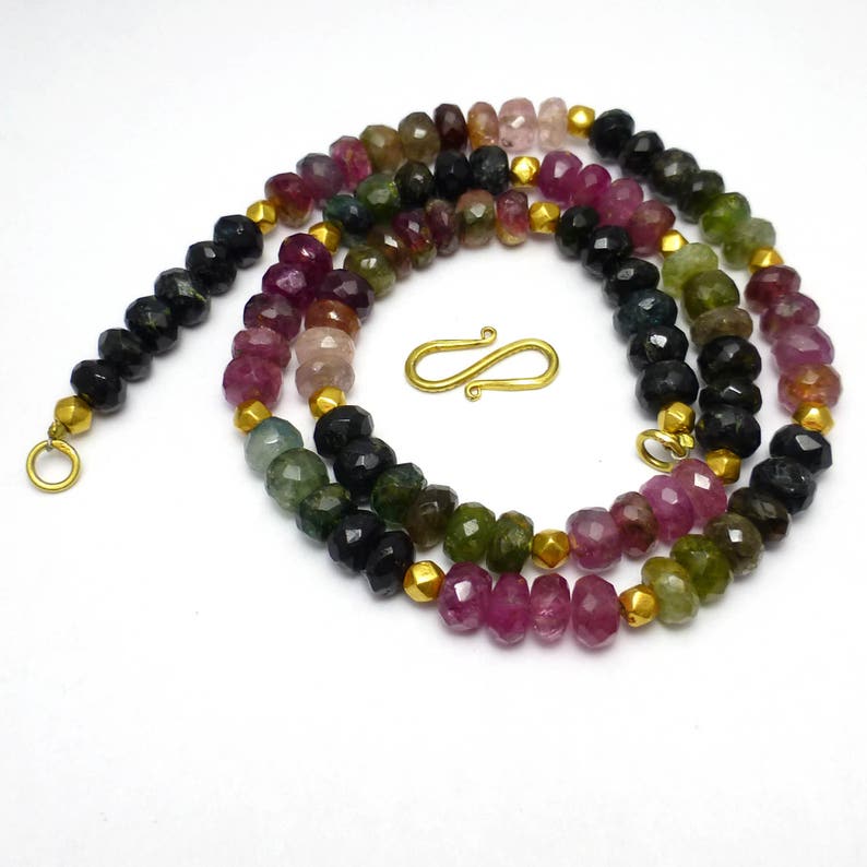 May include: A multi-colored gemstone necklace with a gold clasp. The necklace is made of faceted beads in shades of pink, green, and black.