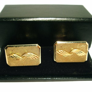 May include: A pair of gold cufflinks in a black box. The cufflinks feature a swirling, wave-like design.