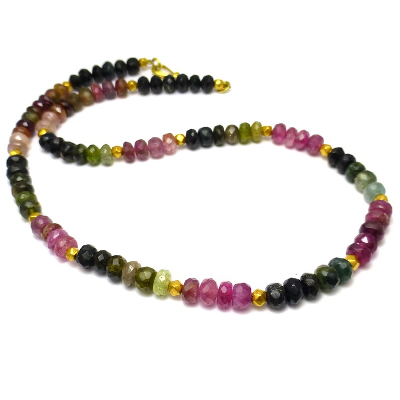 May include: A multi-colored gemstone necklace with black beads and gold accents. The necklace features pink, green, and black gemstones.
