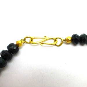 May include: A gold clasp with a black beaded necklace. The clasp is a simple, elegant design with a smooth finish.