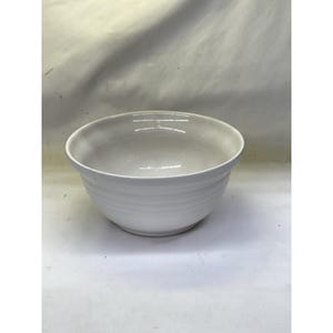 May include: A white ceramic mixing bowl with a wide rim and horizontal ridged detailing around the exterior. The bowl is empty and sits on a white surface.