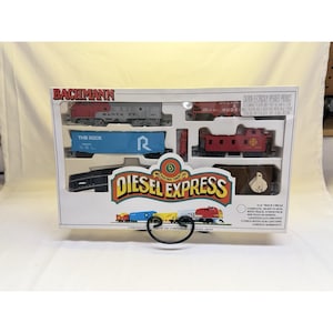 May include: A Bachmann Diesel Express electric train set in a clear plastic box. The set includes a red and silver Santa Fe locomotive, blue freight car, and red caboose. The box features the text "Diesel Express".