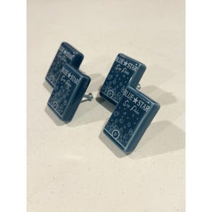Puede incluir: Cuatro pomos rectangulares de cerámica azul oscuro para armarios con un estampado gráfico blanco de burbujas y el texto "BLUE STAR Soap Flakes" con un símbolo de "5¢". Cada pomo tiene un tornillo de montaje metálico.