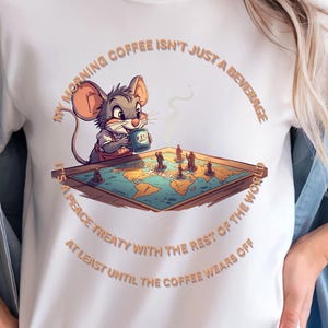 Peut inclure: T-shirt blanc avec une souris de dessin animé buvant du café et jouant aux échecs sur une carte du monde. Le texte dit : "Mon café du matin n'est pas qu'une boisson. C'est un traité de paix avec le reste du monde, du moins jusqu'à ce que le café s'estompe."