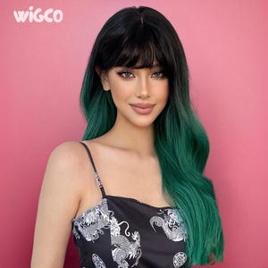 May include: A woman with a black and green wig and a black top with a white dragon design. The wig has a dark fringe and long, wavy, green-tipped hair. The background is a solid pink.