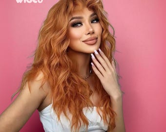 Puede incluir: Una persona con cabello largo, ondulado y castaño rojizo y maquillaje completo, con una parte superior blanca, posa sobre un fondo rosa. El logotipo de WIGCO es visible en la esquina superior izquierda. La mano de la persona está cerca de su rostro.