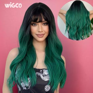 May include: A long, wavy wig with a black to emerald green ombre effect. The wig features a blunt bang and is styled with loose curls. The model is wearing a black top with a white floral design. The Wigco logo is in the top left corner.