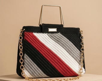 May include: A rectangular crochet handbag featuring diagonal stripes in black, red, white, and gray. The bag includes a gold-tone metal top handle, a matching gold-tone chain shoulder strap, and a small rectangular metal brand plaque on the front.