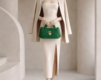 May include: A beige blazer worn over a matching strapless midi dress with a side slit, paired with a dark green crocheted handbag featuring a gold-toned clasp and chain strap. The ensemble is monochromatic, highlighting the textured green bag.