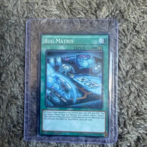May include: A Yu-Gi-Oh! trading card titled Bug Matrix, a green spell card featuring a blue mechanical insect illustration. The card text describes an effect for Insect-Type monsters and Xyz monsters, enclosed in a clear protective plastic sleeve.