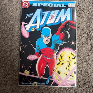 May include: A comic book titled "The Atom Special #1" featuring a superhero in a red, blue, and black costume. The cover art shows the Atom in action against a black background with yellow orbs and pink starbursts. The DC Comics logo is visible.