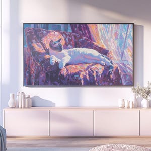 May include: A framed artwork depicts a white and gray cat lounging on a patterned chair. The painting features a vibrant color palette of purples, pinks, and blues. The artwork hangs above a light pink cabinet with white vases and decorative items.