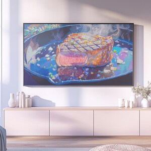 Pode incluir: Uma impressão de arte digital de um bife numa frigideira de ferro fundido. O bife é grelhado com marcas de grelha e vapor a subir. A obra de arte é exibida numa televisão grande com moldura preta, acima de um armário rosa claro.
